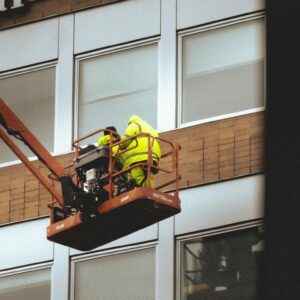 Two workers in yellow working on a sign on the side of a building.