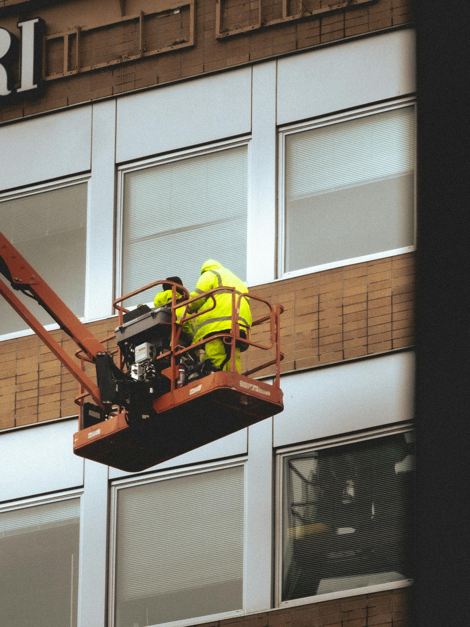 Two workers in yellow working on a sign on the side of a building.